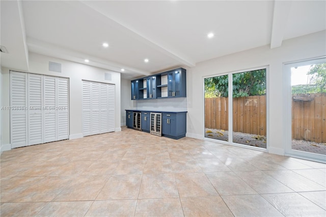 unfurnished living room with beamed ceiling, light tile patterned floors, wine cooler, and bar area