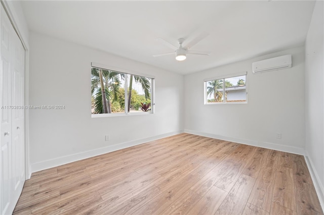 unfurnished room featuring light hardwood / wood-style floors, a wall unit AC, and ceiling fan