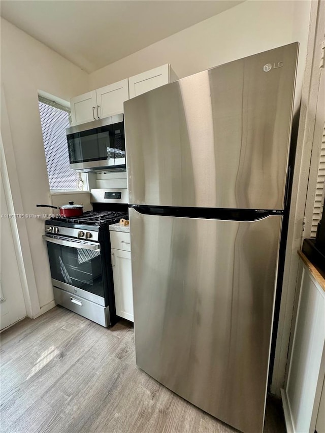 kitchen with stone counters, light hardwood / wood-style floors, white cabinetry, and appliances with stainless steel finishes