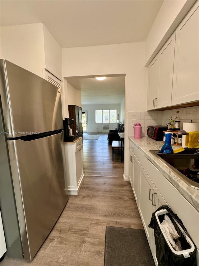 kitchen with stainless steel refrigerator, white cabinetry, decorative backsplash, and light wood-type flooring