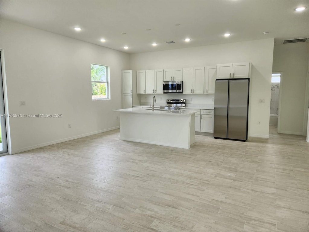 kitchen with white cabinetry, sink, stainless steel appliances, light hardwood / wood-style flooring, and an island with sink