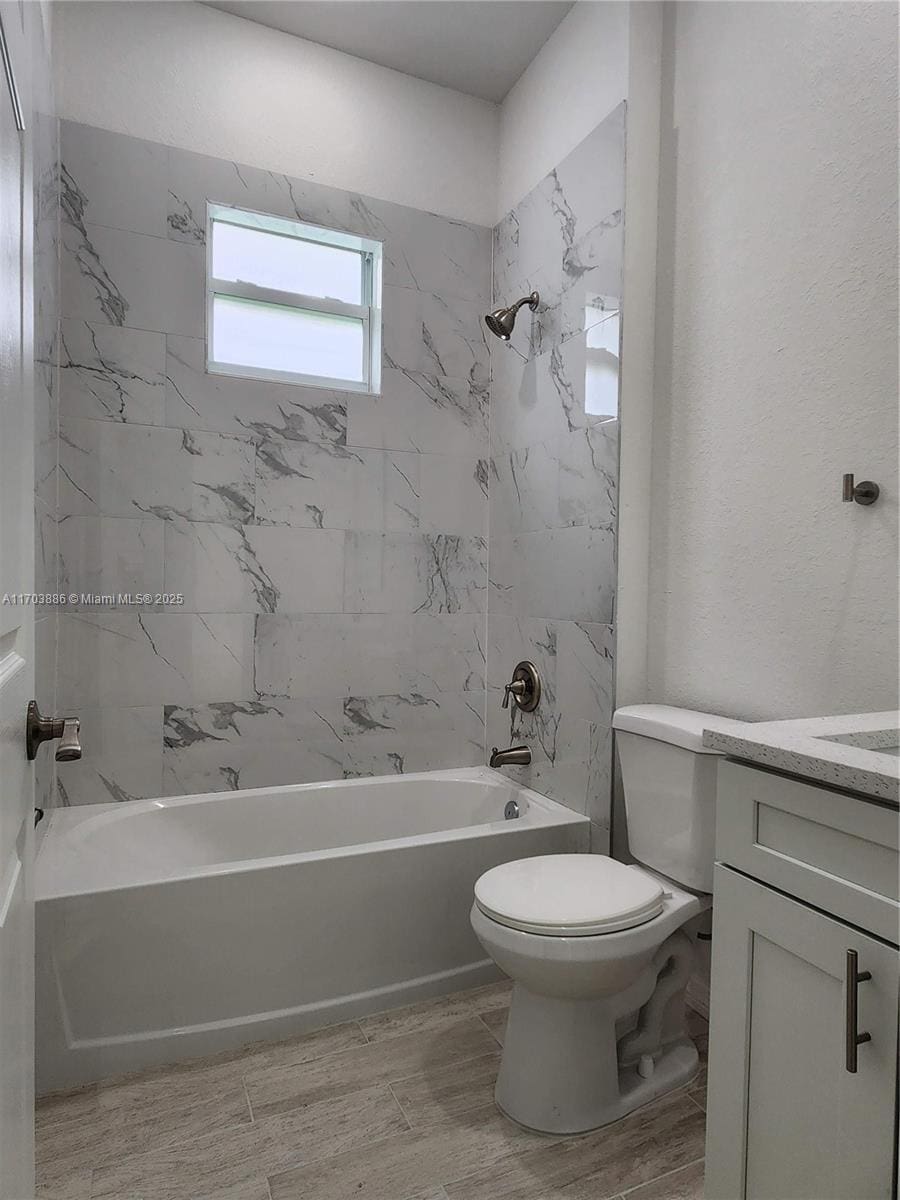 full bathroom featuring vanity, tiled shower / bath combo, and toilet