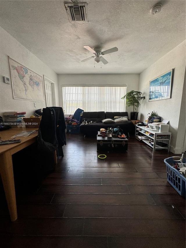 living room with a textured ceiling, ceiling fan, and dark wood-type flooring