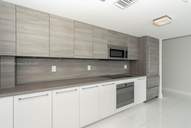 kitchen with decorative backsplash, white cabinets, light tile patterned flooring, and appliances with stainless steel finishes