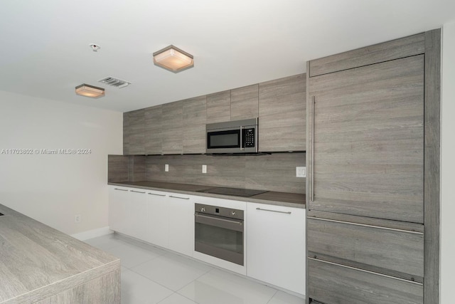 kitchen with tasteful backsplash, white cabinets, light tile patterned floors, and stainless steel appliances