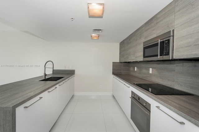 kitchen featuring white cabinetry, sink, light tile patterned floors, and black appliances