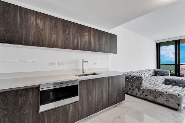 kitchen with stainless steel oven, dark brown cabinetry, and sink