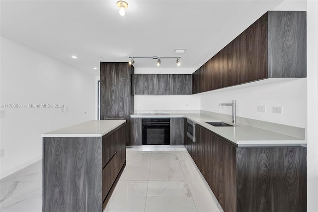 kitchen featuring rail lighting, dark brown cabinets, sink, stovetop, and black oven