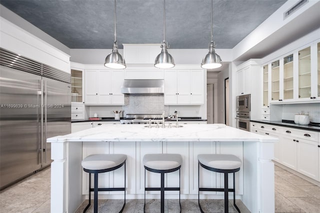 kitchen featuring hanging light fixtures, built in appliances, a center island with sink, and extractor fan