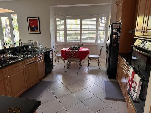 kitchen with dark stone counters, sink, light tile patterned floors, and black appliances