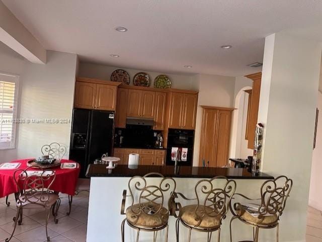 kitchen with kitchen peninsula, a breakfast bar, light tile patterned floors, and black appliances