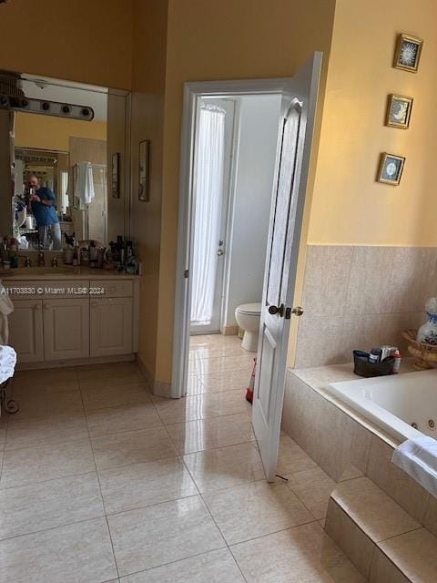 bathroom with tile patterned flooring, vanity, toilet, and tiled tub