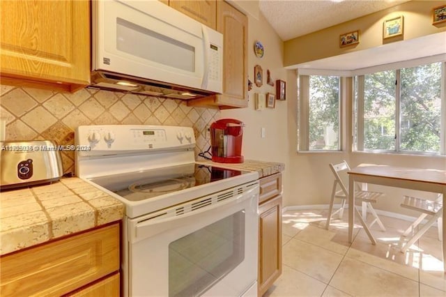 kitchen featuring tile counters, backsplash, a textured ceiling, white appliances, and light tile patterned floors