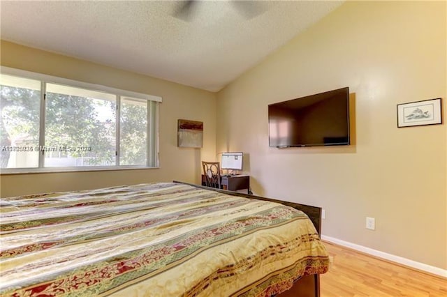 bedroom with a textured ceiling, ceiling fan, light hardwood / wood-style floors, and lofted ceiling