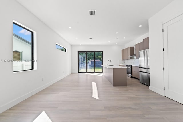 kitchen with a kitchen bar, stainless steel appliances, light hardwood / wood-style flooring, and an island with sink