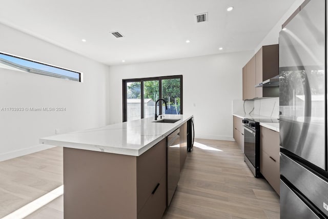 kitchen with light wood-type flooring, appliances with stainless steel finishes, sink, and an island with sink