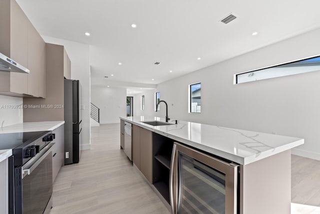 kitchen featuring a kitchen island with sink, sink, wine cooler, appliances with stainless steel finishes, and light hardwood / wood-style floors