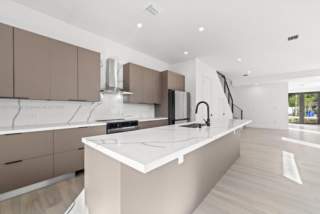 kitchen featuring sink, wall chimney exhaust hood, light wood-type flooring, appliances with stainless steel finishes, and tasteful backsplash