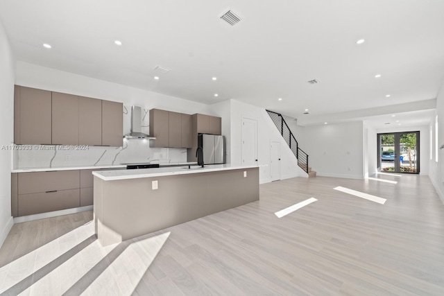 kitchen featuring stainless steel fridge, light hardwood / wood-style floors, a spacious island, and wall chimney range hood