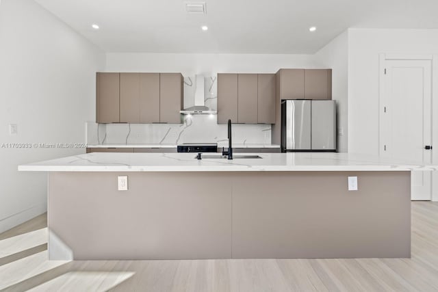 kitchen featuring wall chimney range hood, sink, stainless steel fridge, light wood-type flooring, and a large island