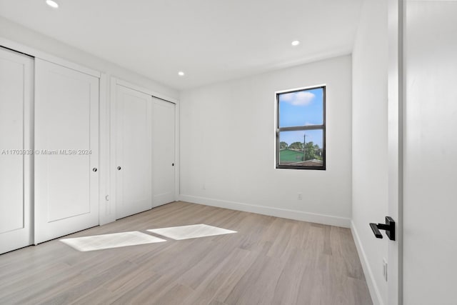 unfurnished bedroom featuring light wood-type flooring and multiple closets