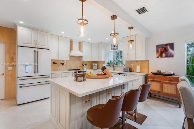 kitchen featuring premium range hood, backsplash, an island with sink, pendant lighting, and high end fridge