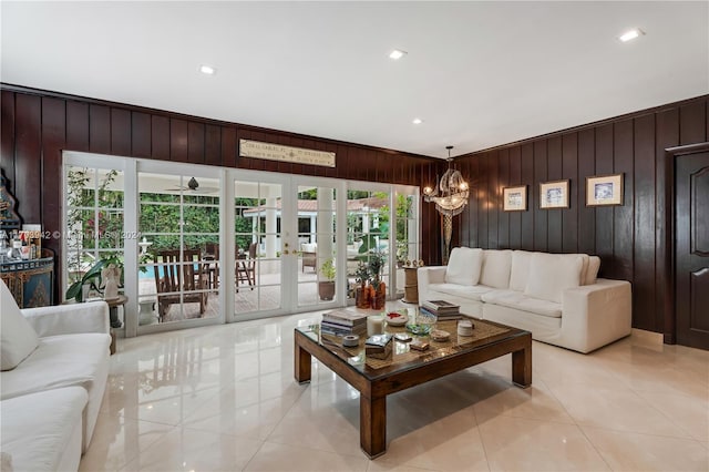 tiled living room with ceiling fan with notable chandelier, wood walls, and french doors