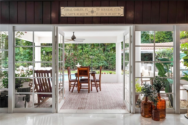 doorway with ceiling fan, plenty of natural light, light tile patterned floors, and wooden walls