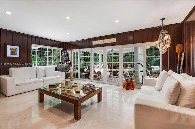 tiled living room with wooden walls, french doors, crown molding, and a notable chandelier