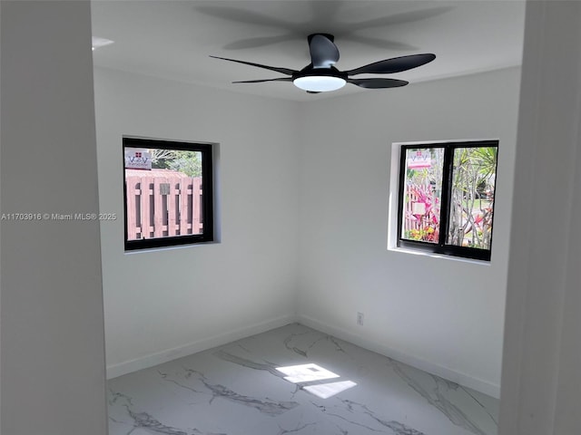 spare room with marble finish floor, plenty of natural light, baseboards, and a ceiling fan