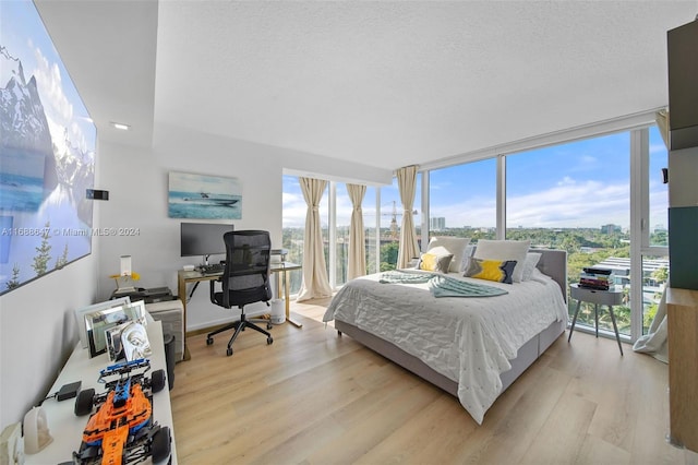 bedroom featuring multiple windows, light hardwood / wood-style flooring, a textured ceiling, and a wall of windows