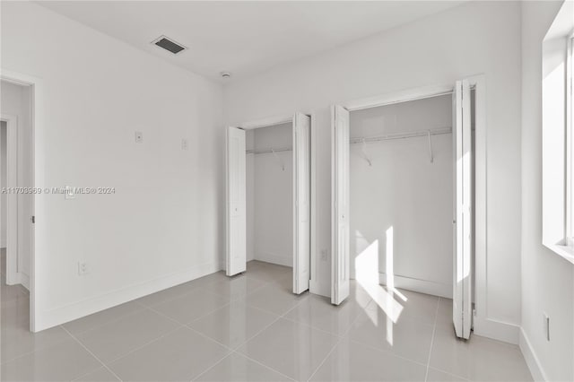 unfurnished bedroom featuring light tile patterned floors and two closets