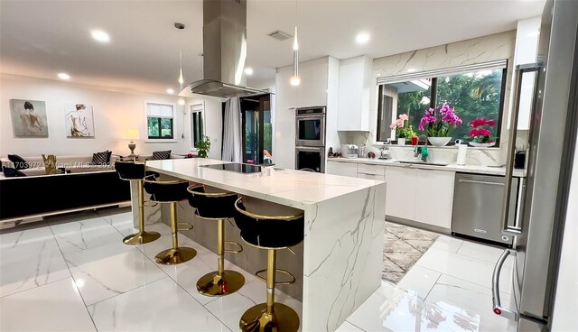 kitchen featuring light stone countertops, island range hood, stainless steel appliances, a kitchen island, and white cabinetry