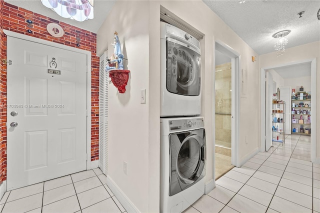 laundry room with light tile patterned floors, a textured ceiling, stacked washer and dryer, and brick wall