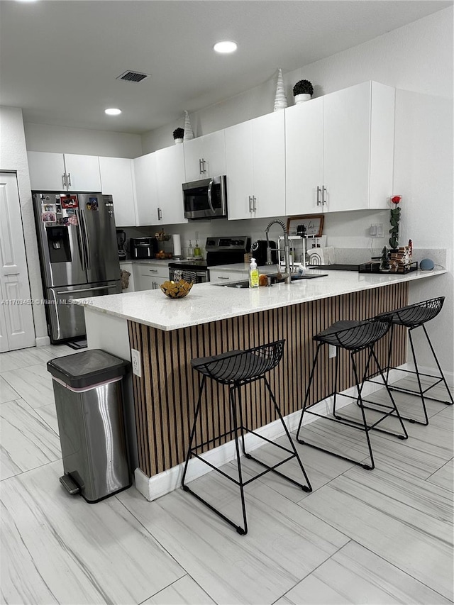 kitchen featuring a kitchen bar, white cabinetry, kitchen peninsula, and appliances with stainless steel finishes