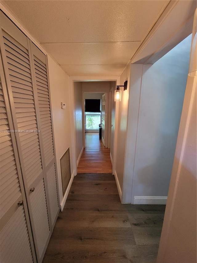 corridor with a textured ceiling and dark wood-type flooring