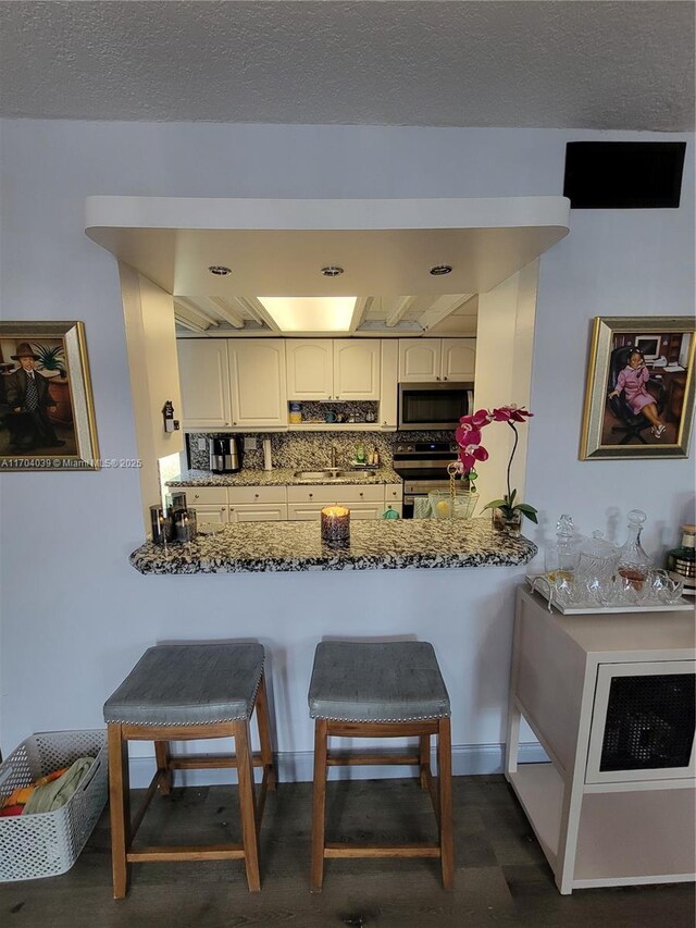 kitchen featuring a kitchen breakfast bar, stone countertops, white cabinetry, kitchen peninsula, and stainless steel appliances