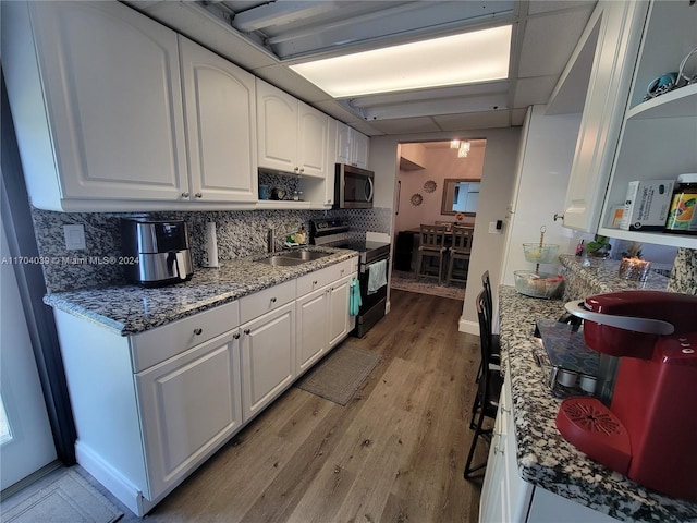 kitchen with stainless steel appliances, tasteful backsplash, light hardwood / wood-style flooring, dark stone countertops, and white cabinets