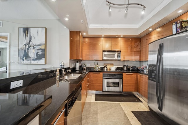 kitchen with appliances with stainless steel finishes, a tray ceiling, sink, dark stone countertops, and light tile patterned flooring