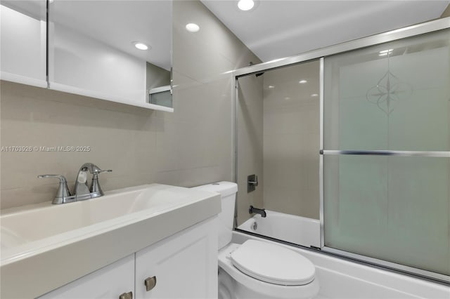 full bathroom with vanity, tile walls, shower / bath combination with glass door, and toilet