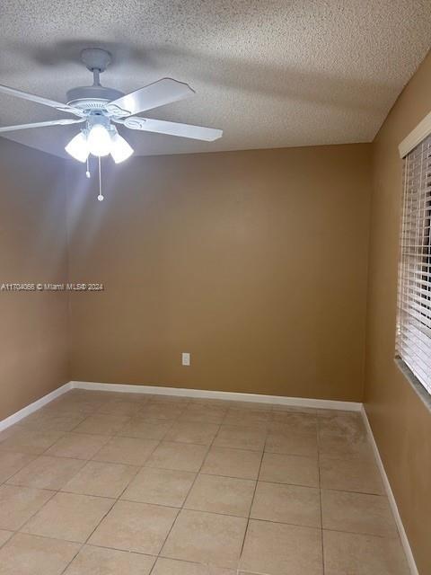 tiled empty room featuring ceiling fan and a textured ceiling