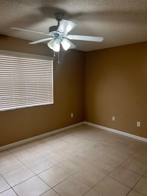 empty room featuring ceiling fan, light tile patterned floors, and a textured ceiling