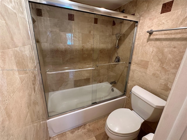 bathroom with toilet, tile walls, and bath / shower combo with glass door