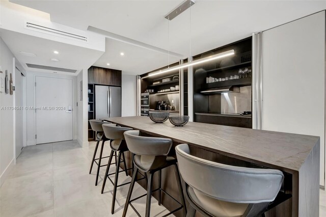 kitchen featuring stainless steel fridge, dark brown cabinets, hanging light fixtures, and a breakfast bar area