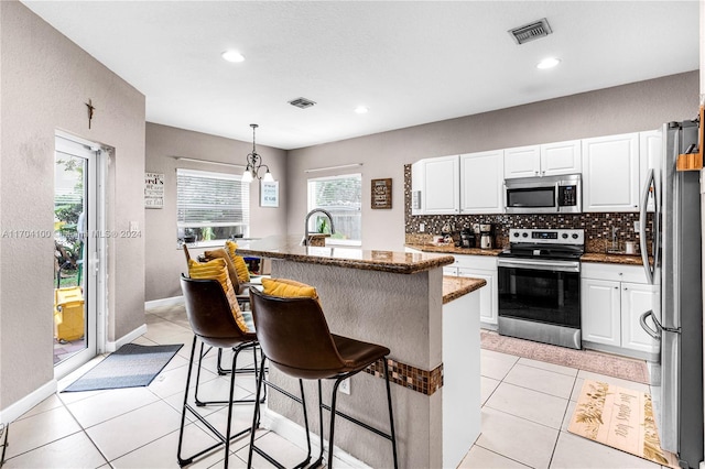 kitchen featuring hanging light fixtures, stainless steel appliances, a breakfast bar area, a kitchen island with sink, and white cabinets