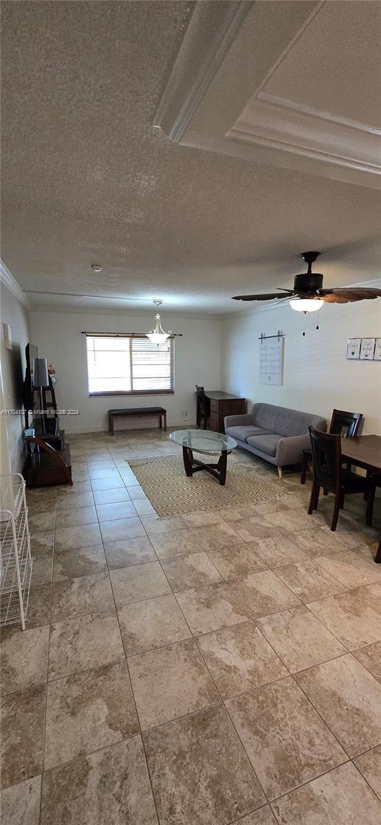 unfurnished living room featuring a textured ceiling, ceiling fan with notable chandelier, and crown molding