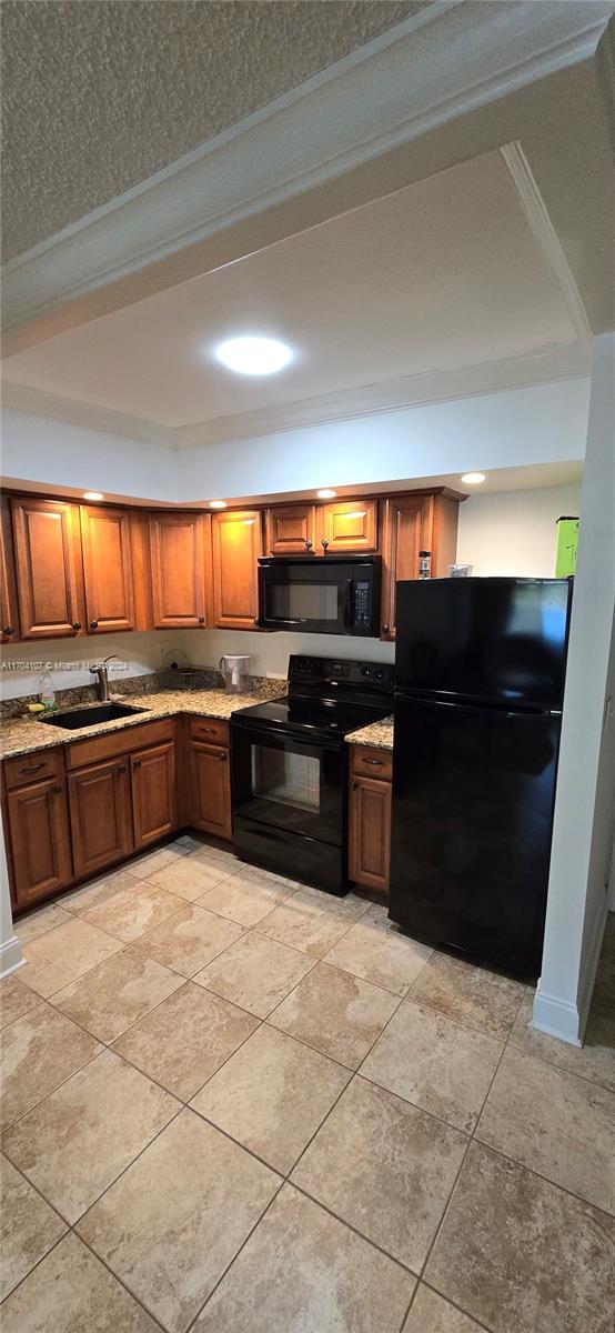 kitchen with a raised ceiling, sink, black appliances, and ornamental molding