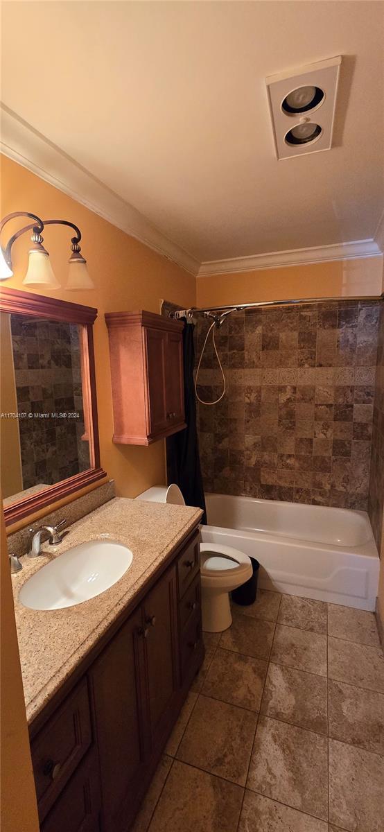 full bathroom featuring tile patterned floors, ornamental molding, vanity, tiled shower / bath combo, and toilet