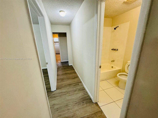 bathroom featuring hardwood / wood-style floors, tiled shower / bath combo, a textured ceiling, and toilet