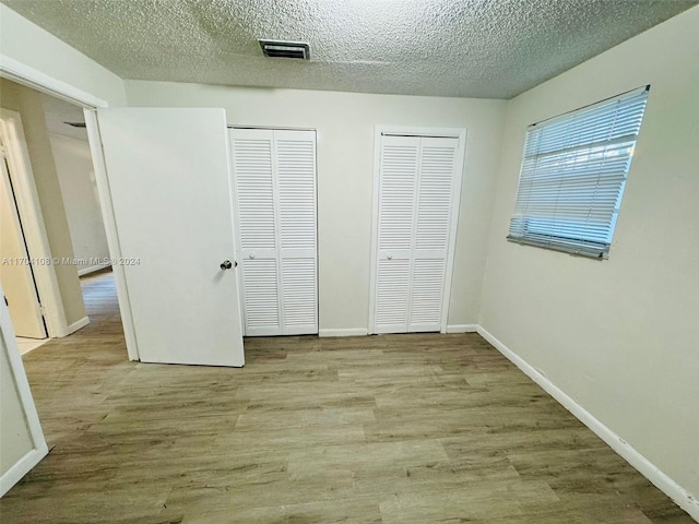 unfurnished bedroom featuring a textured ceiling, light wood-type flooring, and two closets